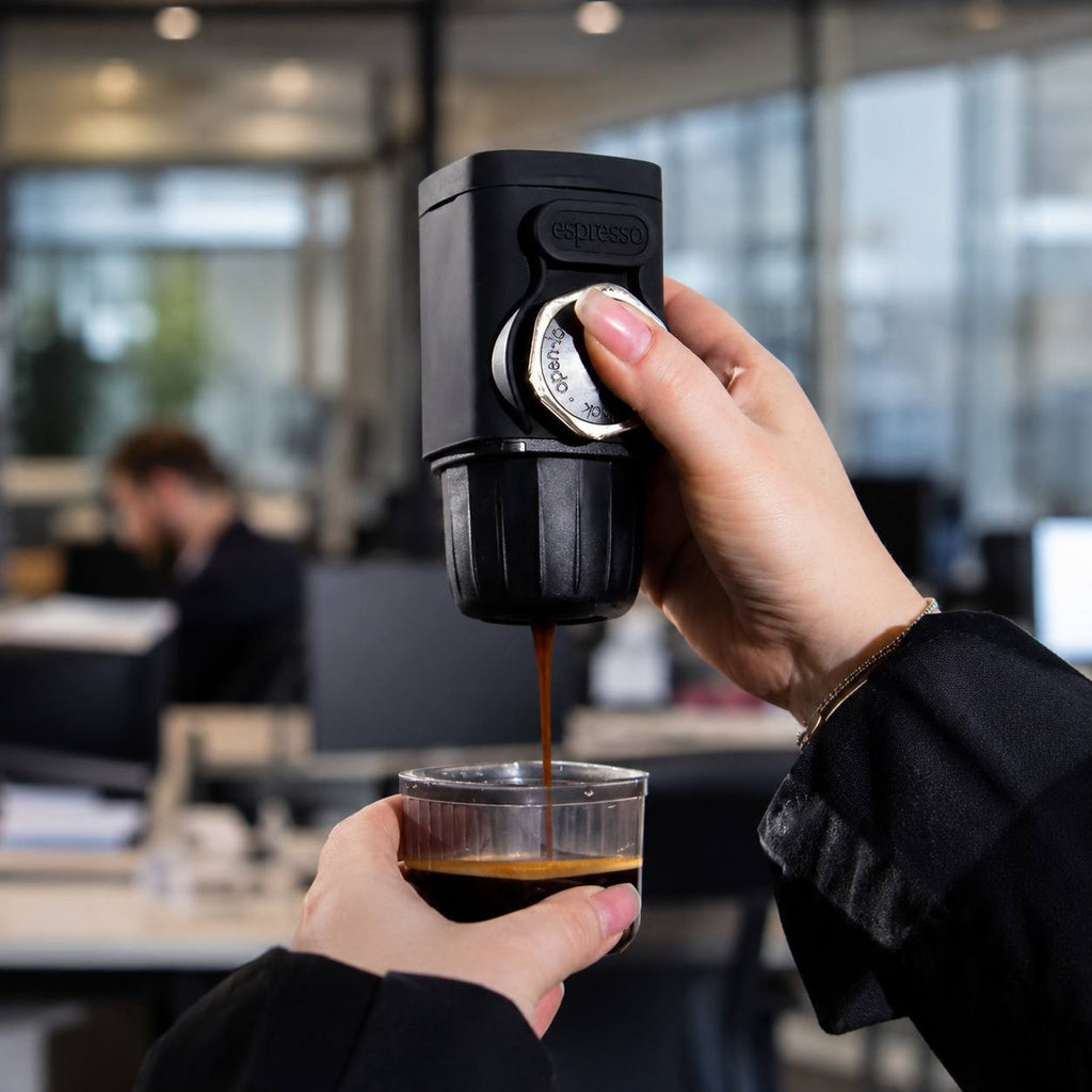 Close-up of a person operating a handheld portable espresso machine to brew fresh coffee.