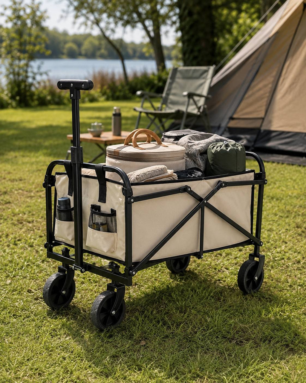 Beige collapsible utility wagon loaded with bags and camping gear, set up on grass at a campsite with a lake and forest in the background.