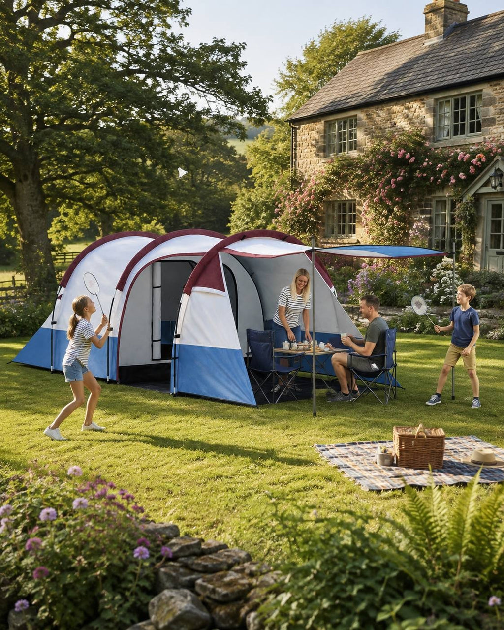 Family playing badminton in the garden of a stone house next to a blue, white, and burgundy camping tent with an extended canopy.
