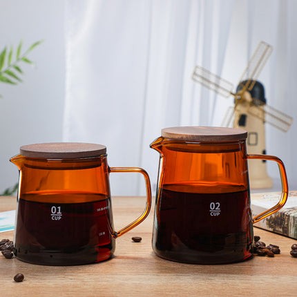 Two amber-colored glass coffee pots with wooden lids on a wooden surface, with a windmill decoration in the background.