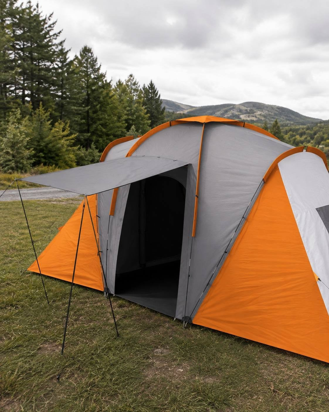 Close-up view of the entrance and extended front canopy of a large orange, grey, and white multi-room camping tent set up on grass near a forest.