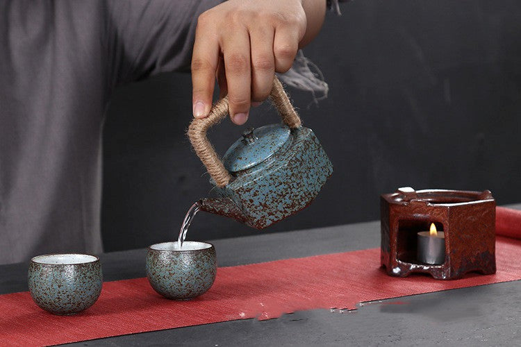 Tea ceremony with a teapot, cups, and candle on a red mat.