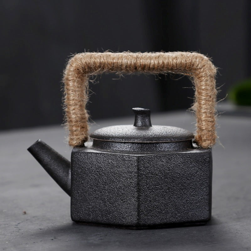 Black textured teapot with a jute handle on a dark background