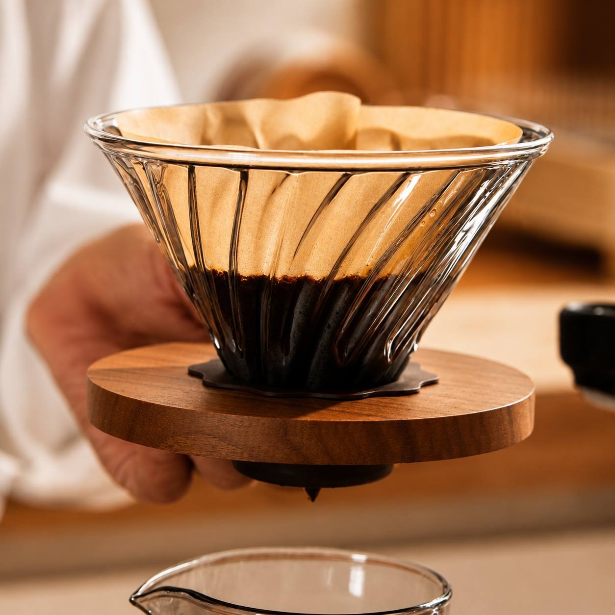 A close-up view of a glass coffee dripper with a paper filter and coffee grounds being held by a person.