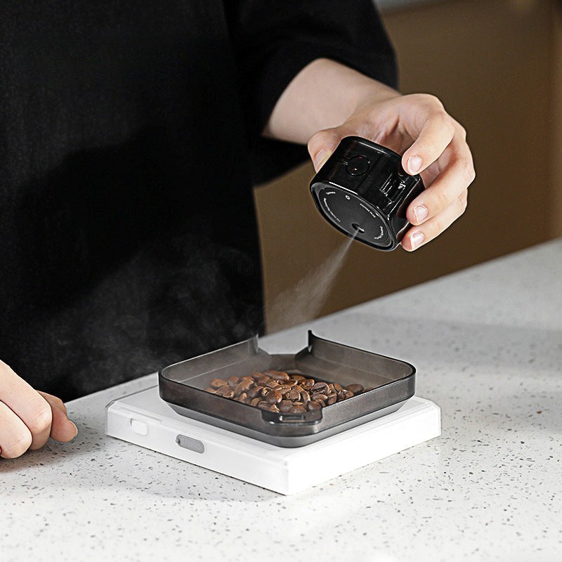 Person using a small black device to dispense coffee beans onto a digital scale.