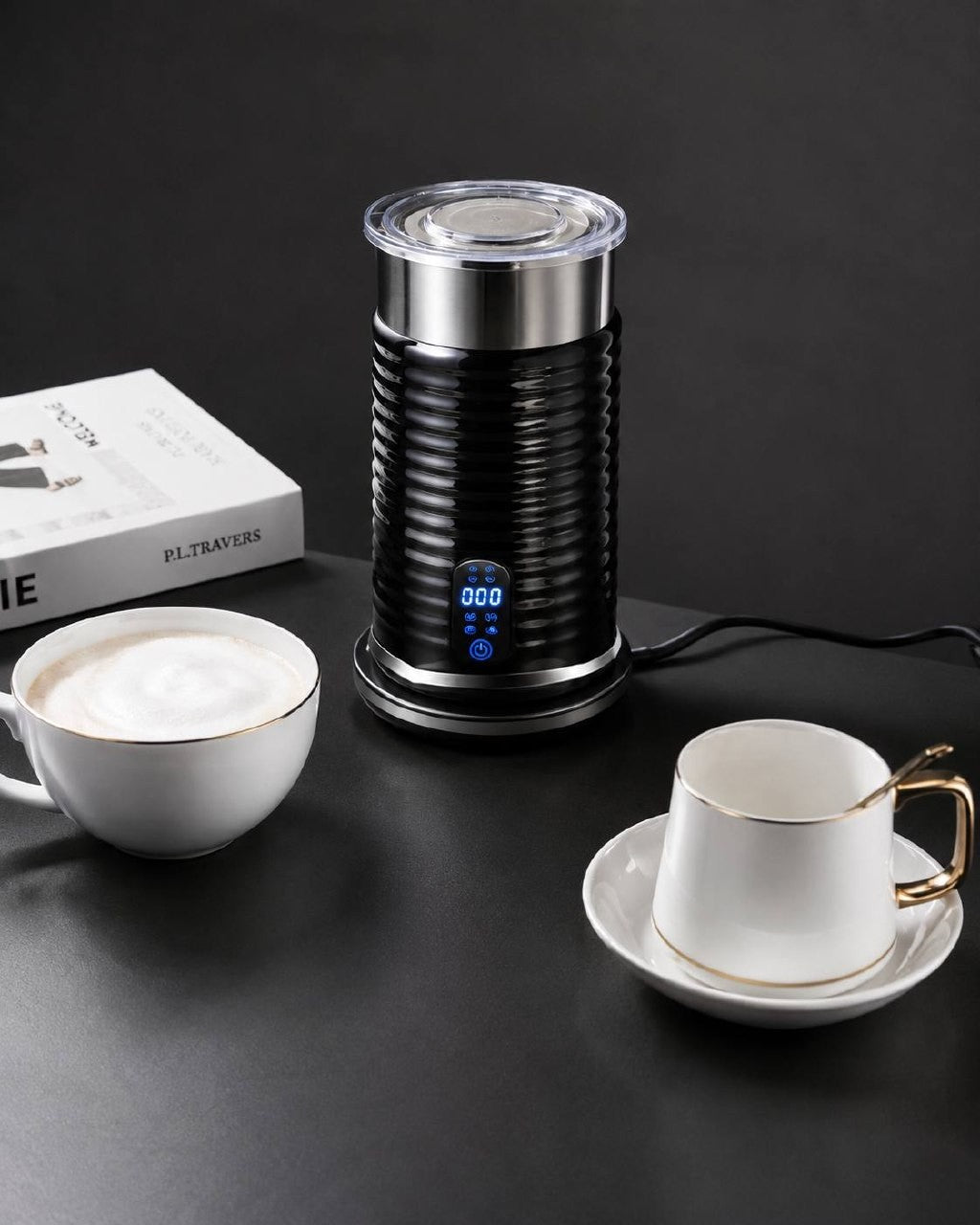 Electric milk frother set up on a dark marble table next to coffee cups for a home cafe.