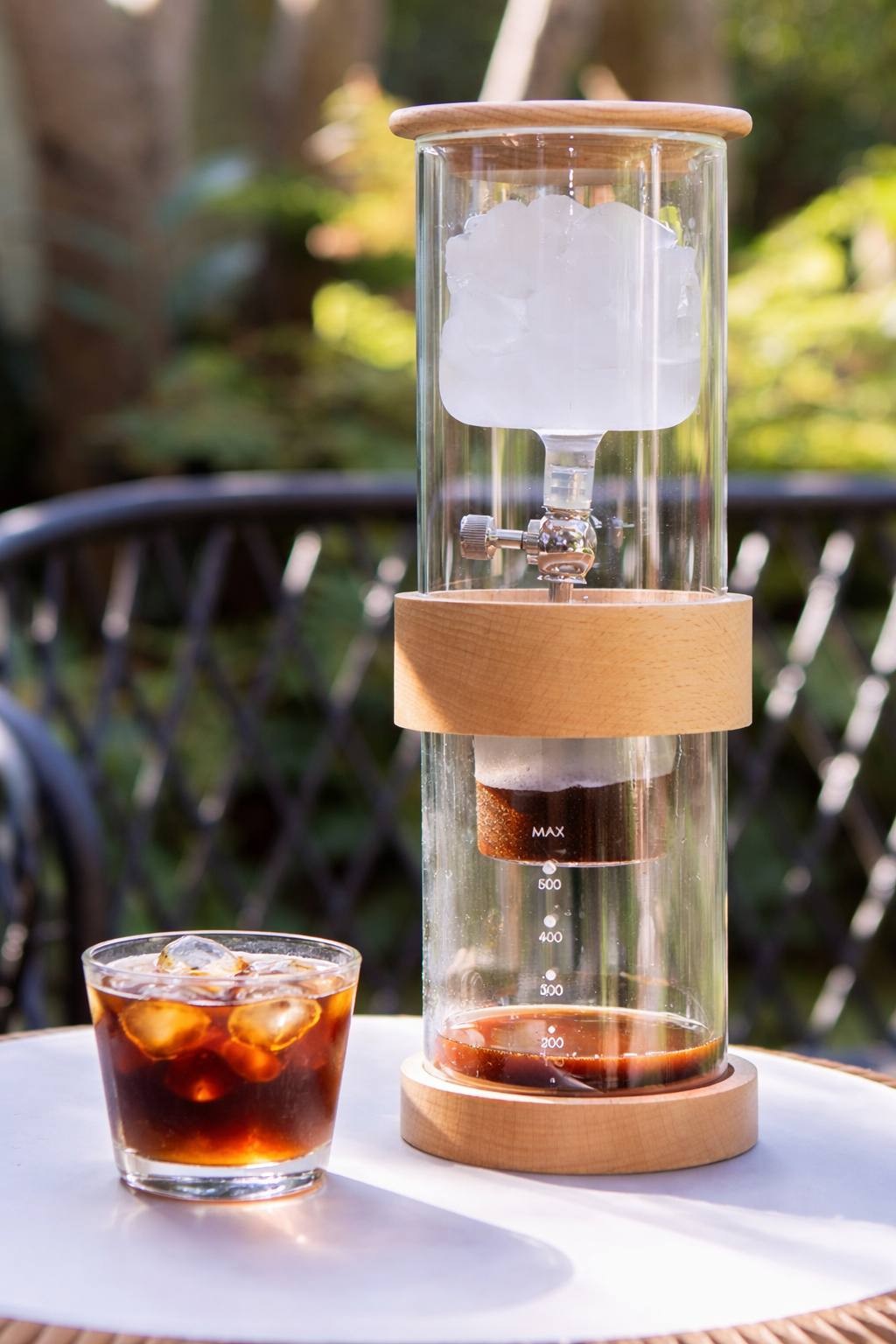 Clear ice drip coffee brewer tower extracting fresh cold brew coffee on an outdoor table during a sunny day