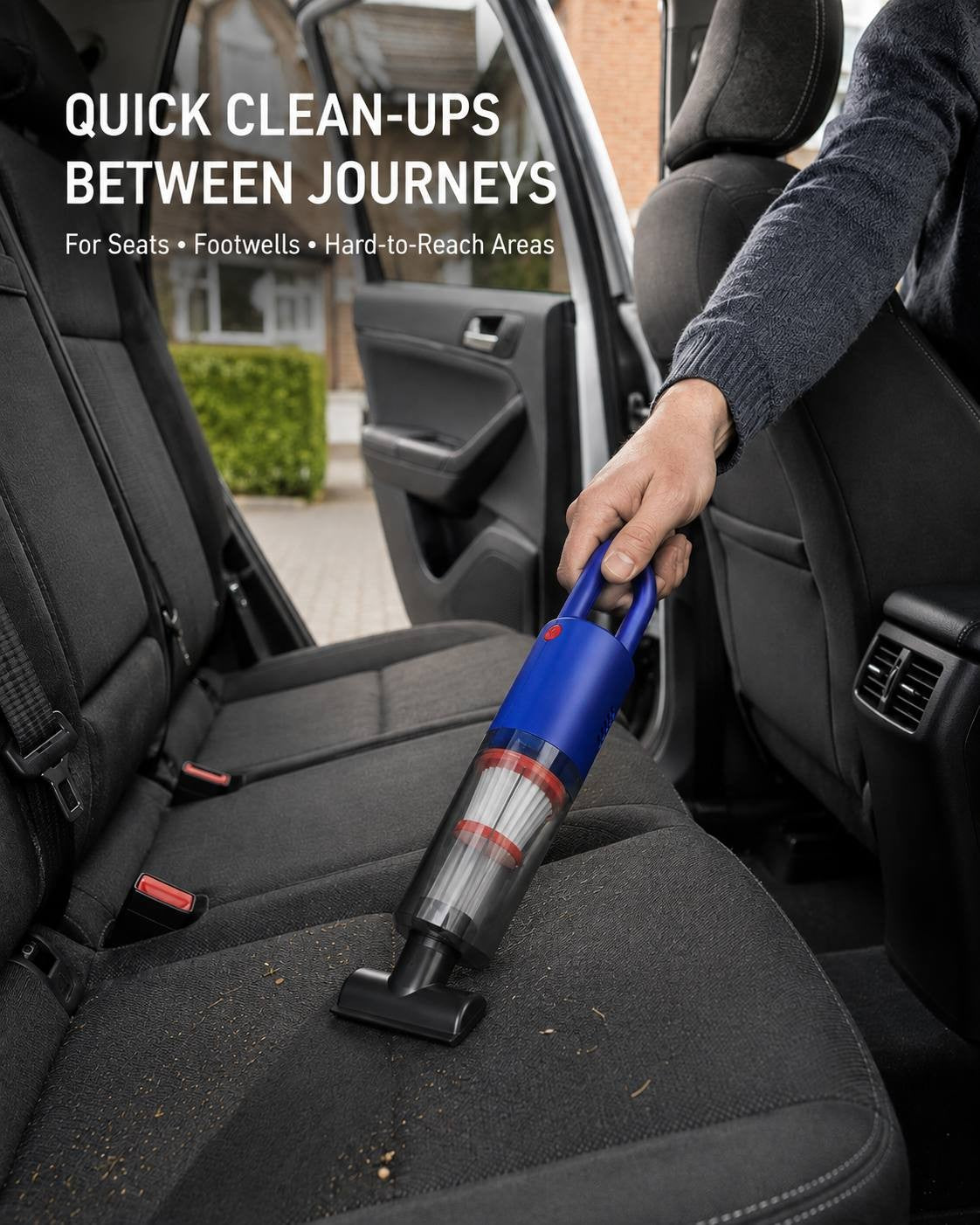 A person using a blue portable handheld vacuum cleaner equipped with a flat nozzle attachment to clean debris from the dark fabric back seats of a car.