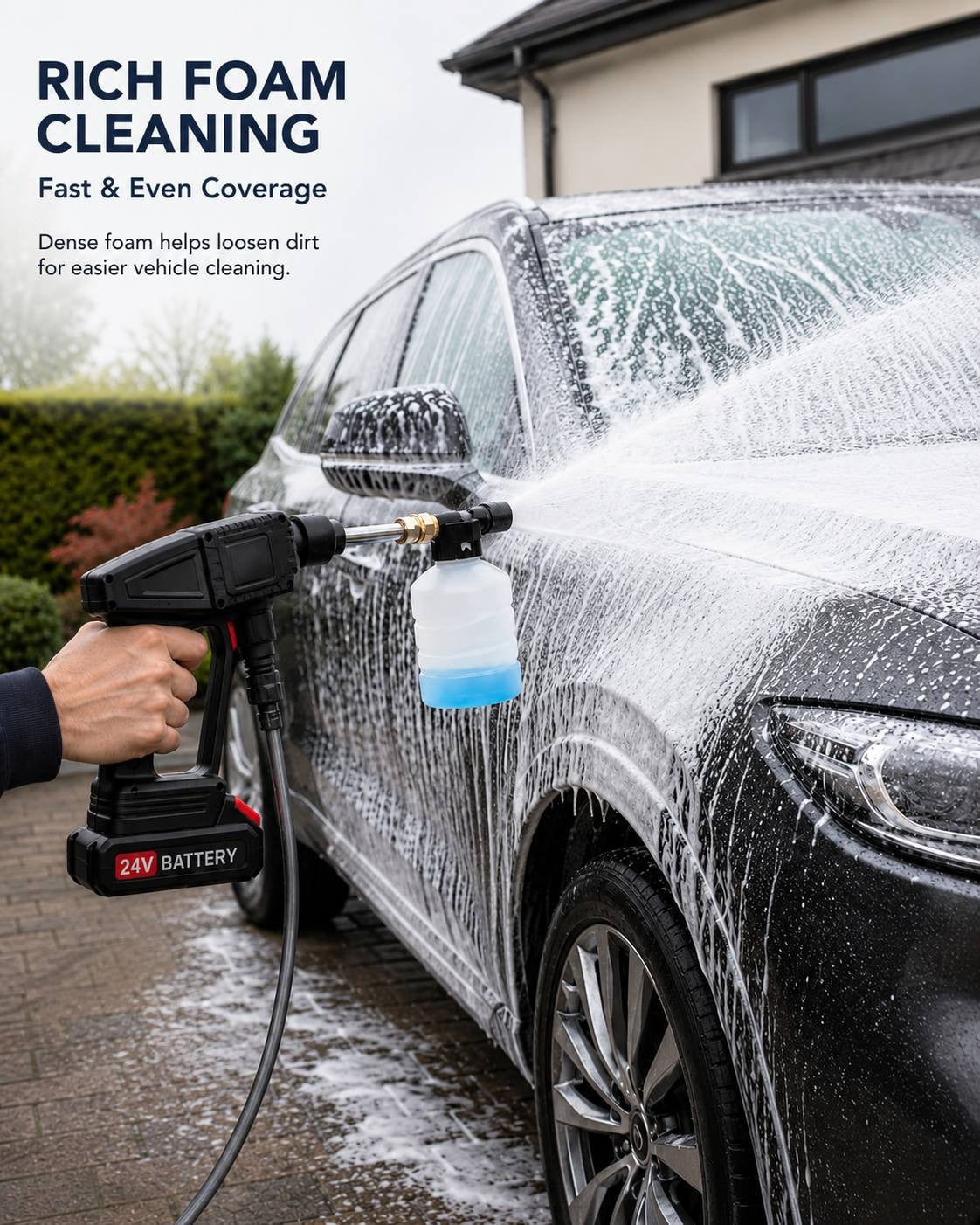 A close-up action shot of a person using a 24V cordless pressure washer with an attached soap foam bottle to apply a thick layer of cleaning foam across the side and door of a dark grey car.