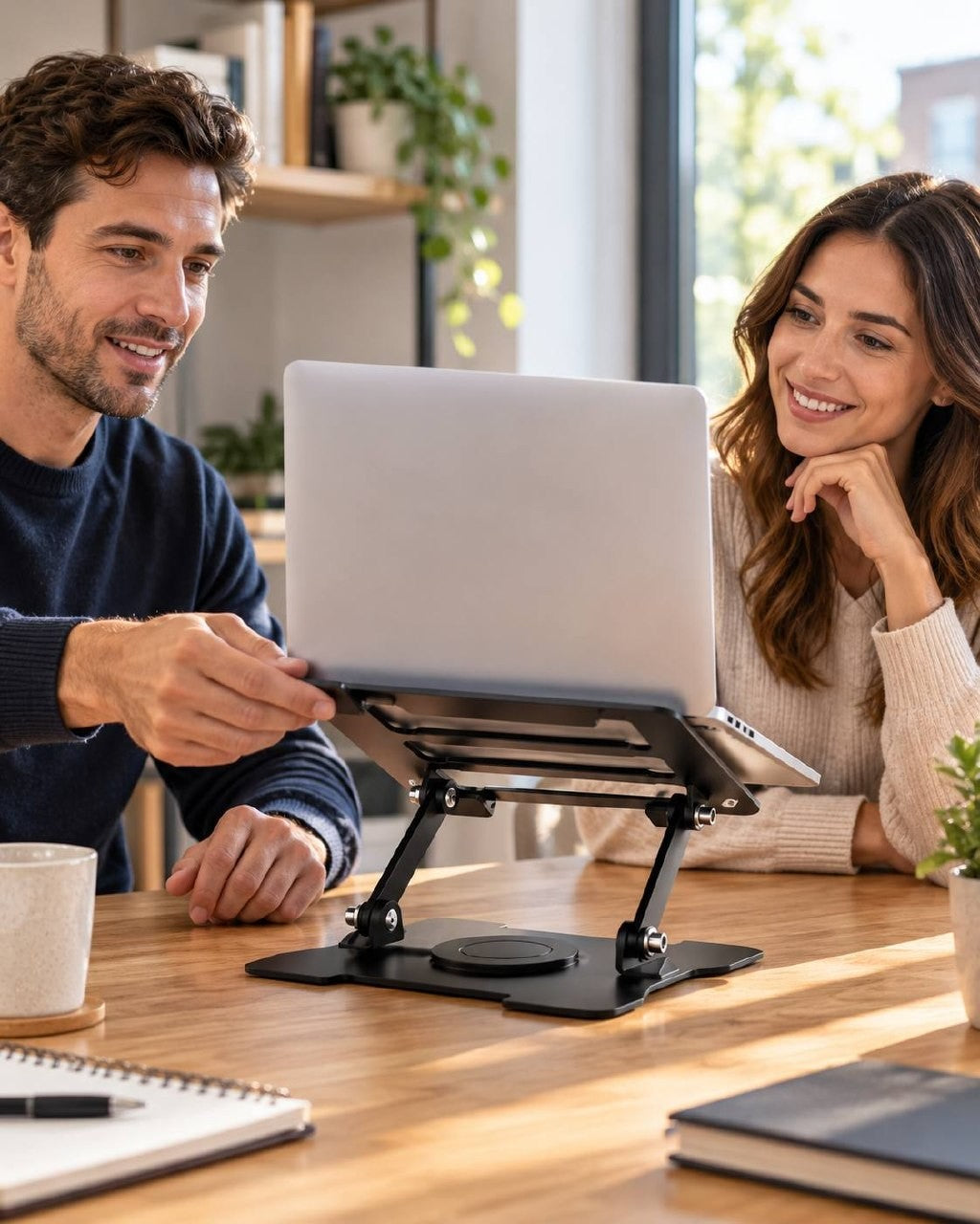 A smiling man and woman collaborating together around a desk, using a rotating laptop stand to swivel the screen toward each other.