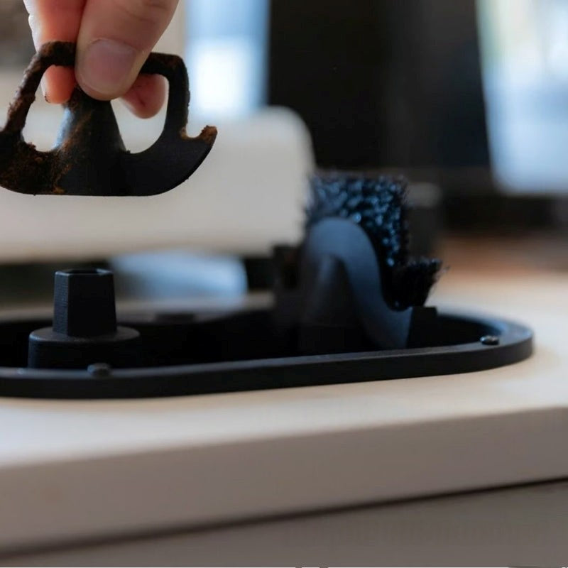 Person using a black hair clipper on a white appliance with blurred background
