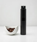 Black spray bottle next to a bowl of coffee beans on a white background