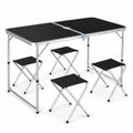 Folding camping table with a black top and aluminum frame, accompanied by four folding black stools, isolated on a white background.