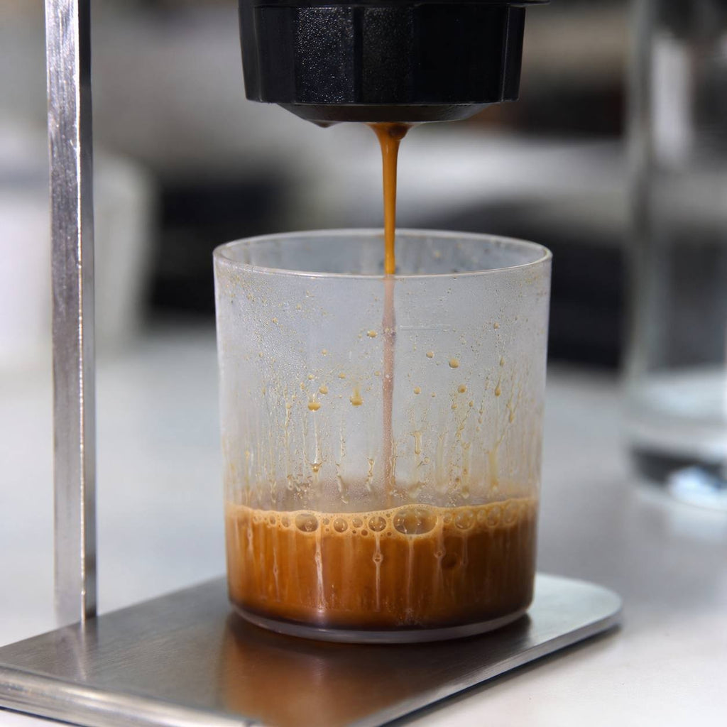 Close-up of fresh aromatic espresso pouring from a portable coffee maker into a glass cup.