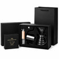 A complete coffee brewing kit including a box of filters, a dripper, a grinder, a kettle, and a gift bag on a white background.