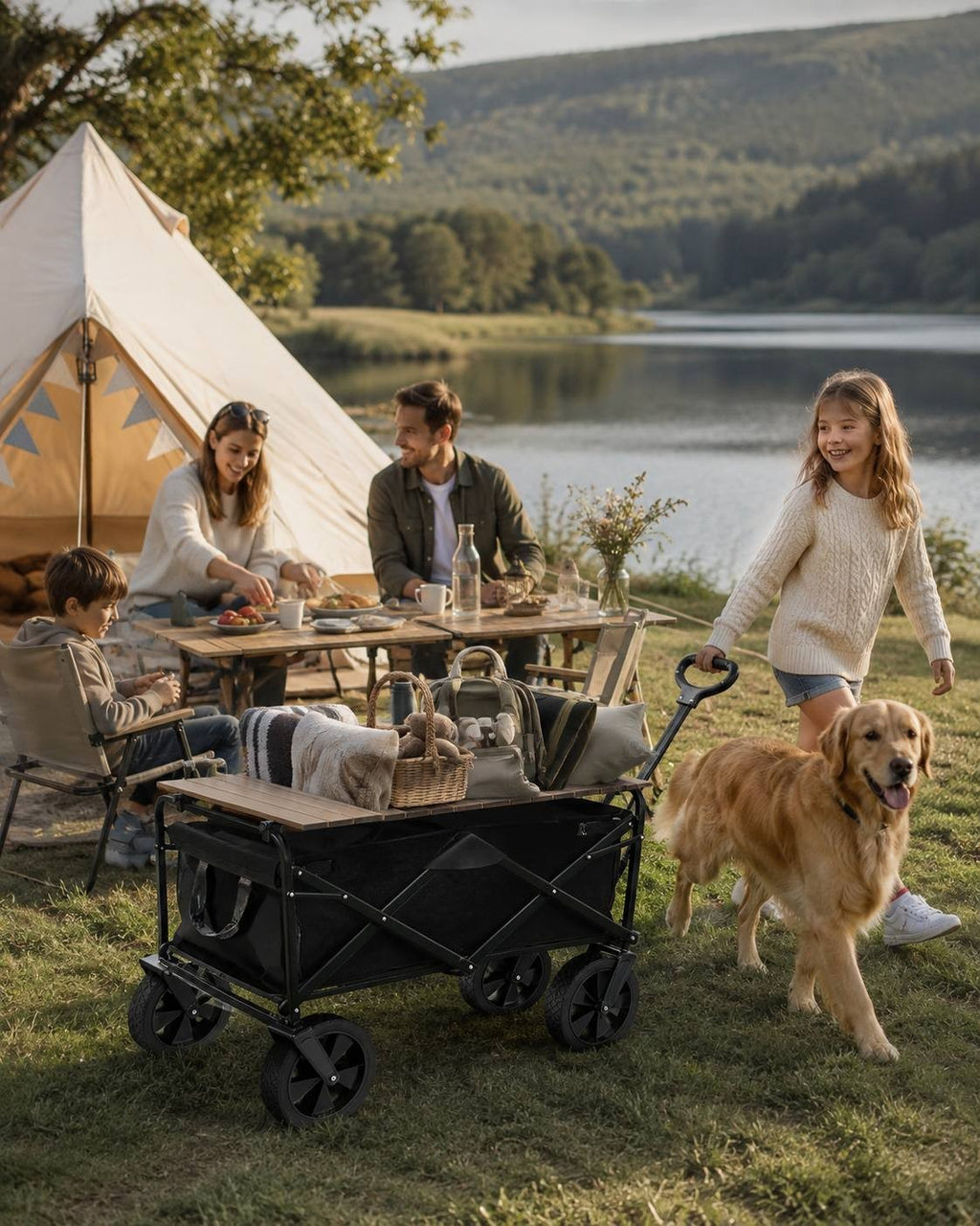 Young girl pulling a black folding utility wagon filled with blankets near a tent, family picnic table, and dog by a lake.