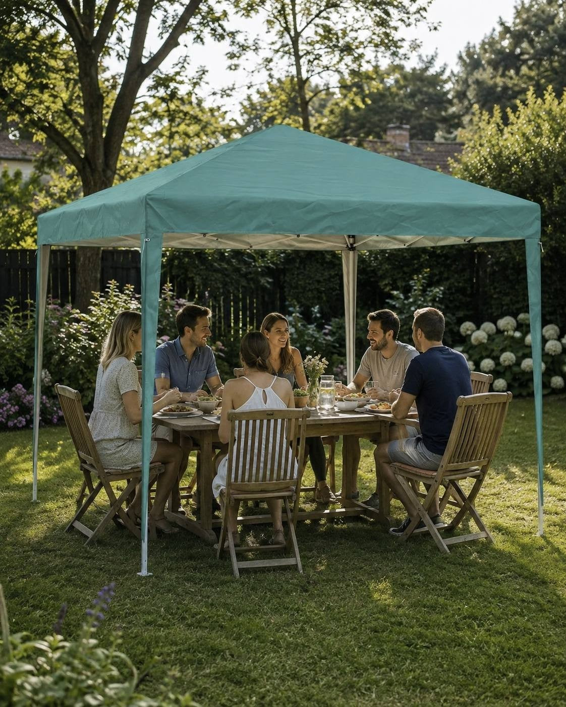 Group of people sitting around a wooden dining table having a meal under a green pop-up gazebo set up in a sunny garden.