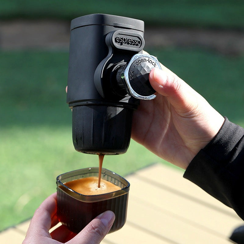  portable espresso maker to pour coffee into a small cup outdoors.