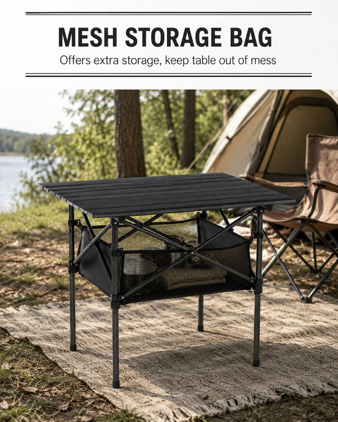 A black folding camping table with items stored in its under-table mesh bag, set up on a mat near a tent by a lake in a forest campsite.