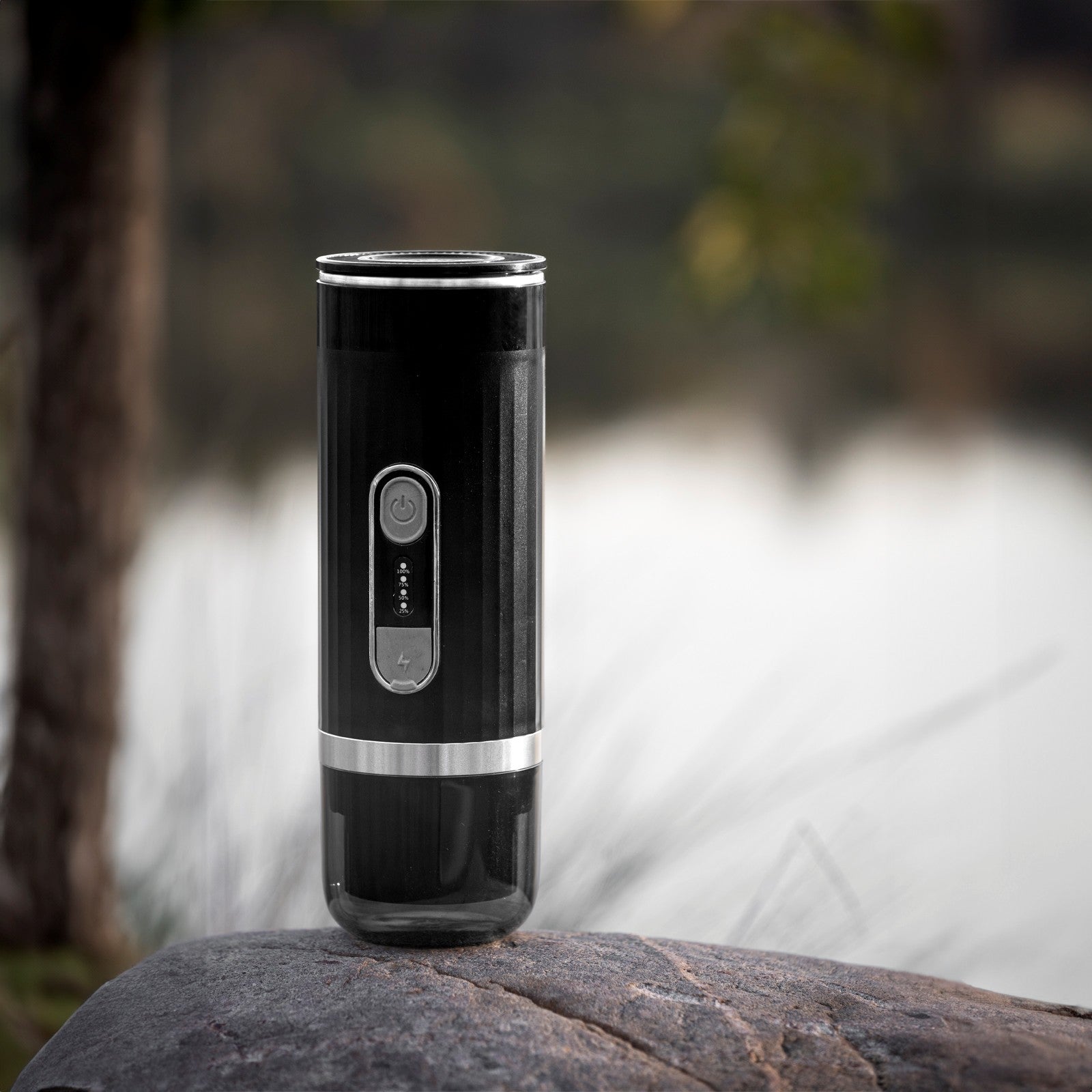Sleek black portable electric espresso machine standing on a large stone with a blurred nature background