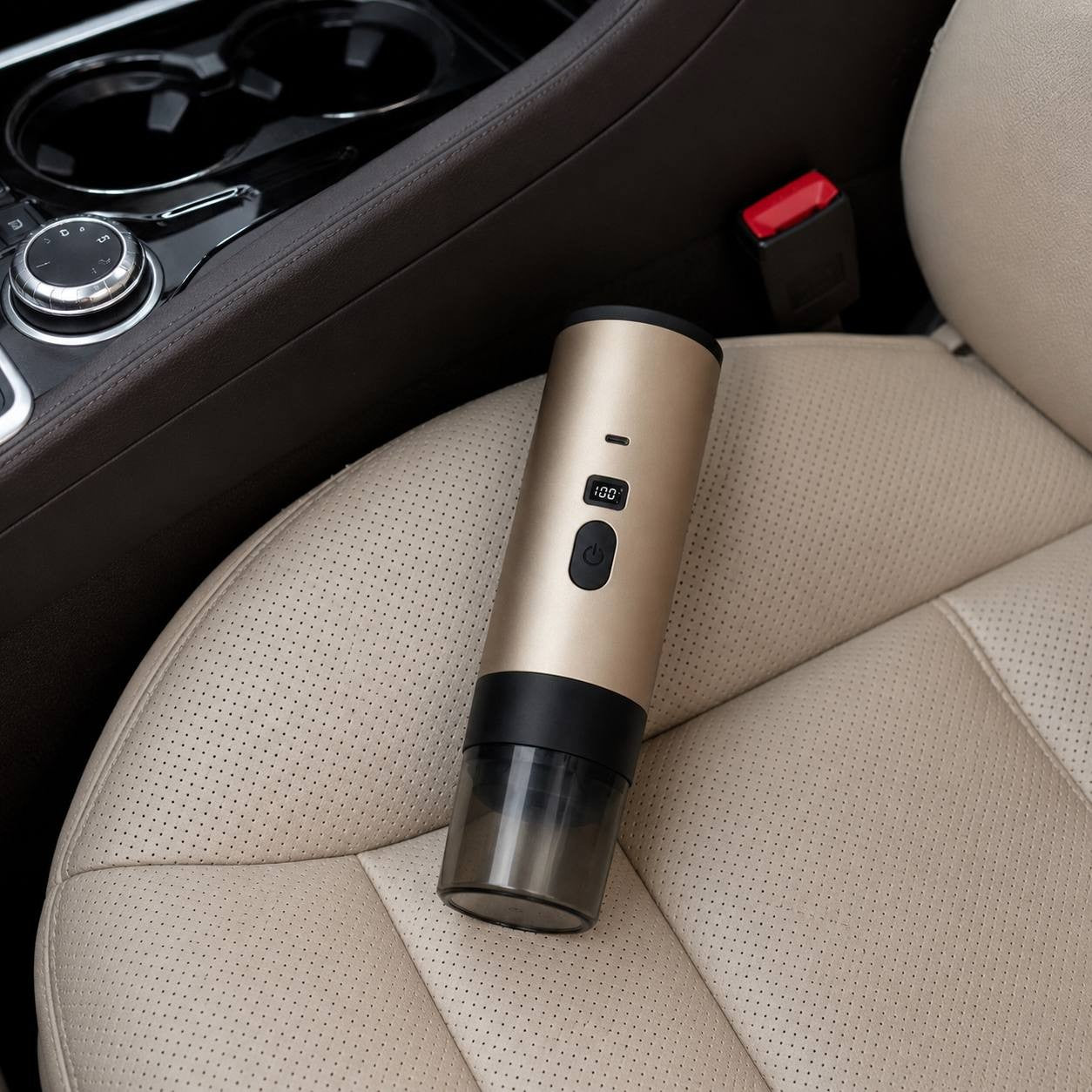 Wireless portable electric espresso maker with a golden metallic body and digital display sitting on a beige leather car seat.