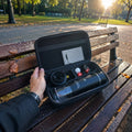 Portable espresso machine inside its protective travel carrying case, resting on a park bench.