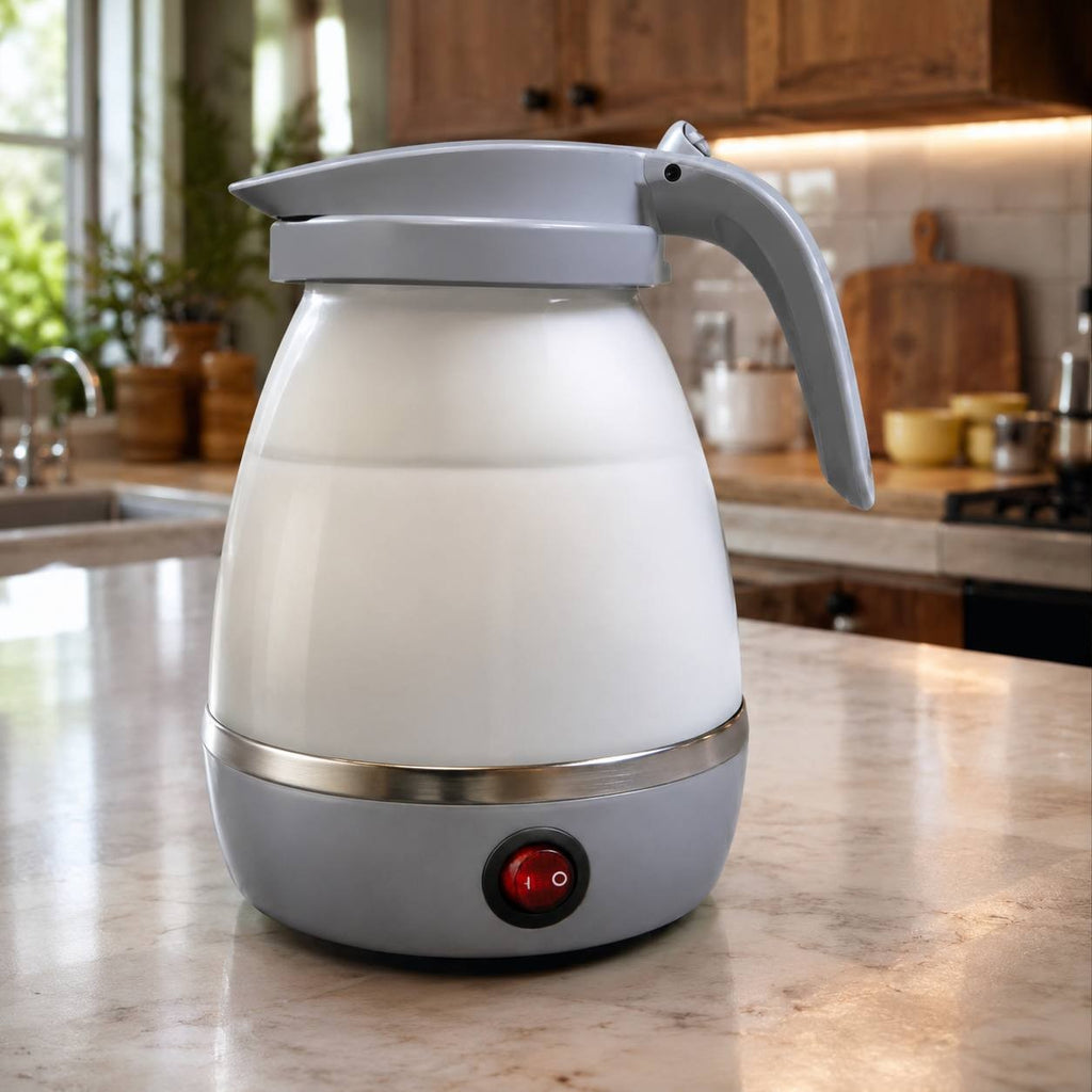 Foldable electric travel kettle made of grey and white silicone, shown sitting on a marble kitchen countertop with wooden cabinets in the background.