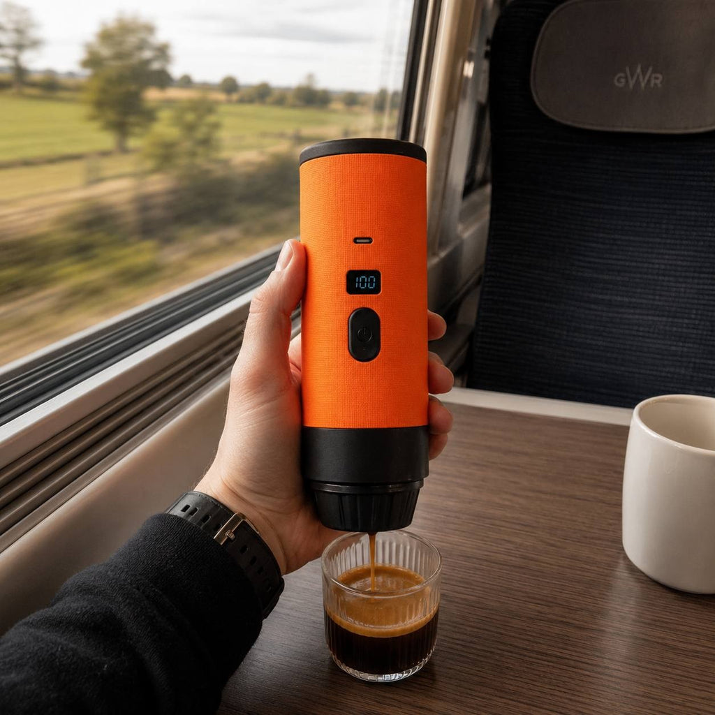 Hand holding an orange portable espresso maker while brewing coffee on a train journey.