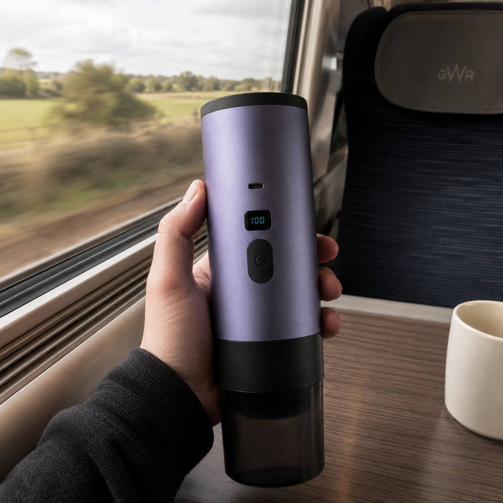 Hand holding a purple portable espresso maker inside a train cabin with a blurred landscape view.