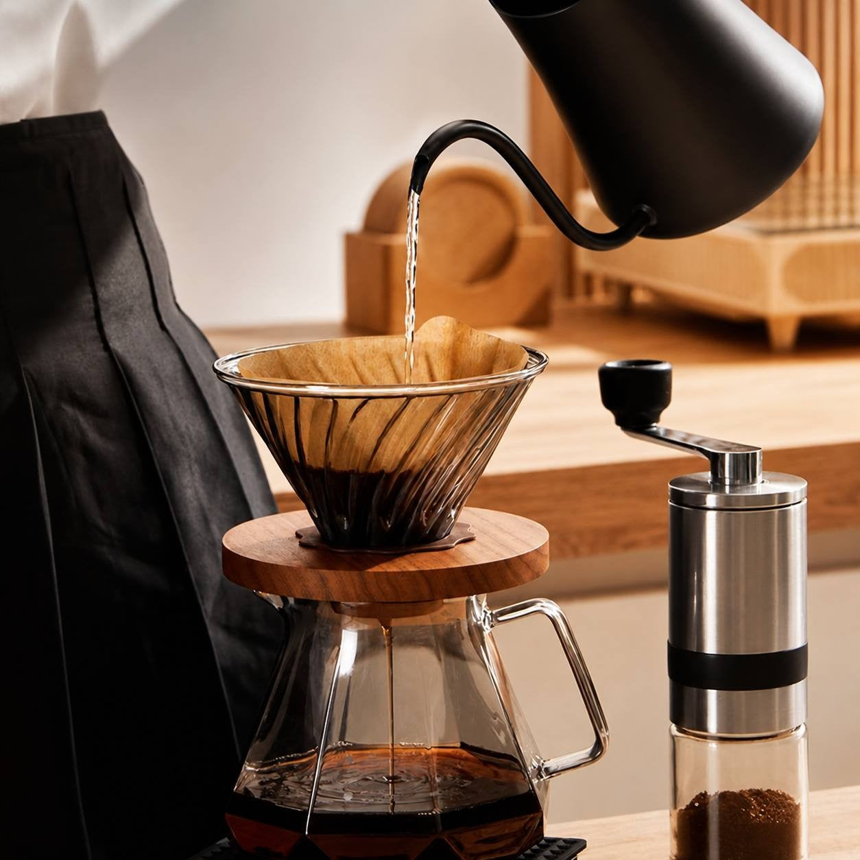 A person pouring hot water from a gooseneck kettle into a glass coffee dripper set on a counter.