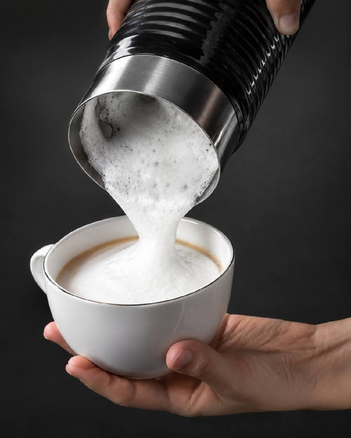 Action shot of pouring dense white milk foam from the automatic frother into a glass coffee cup.
