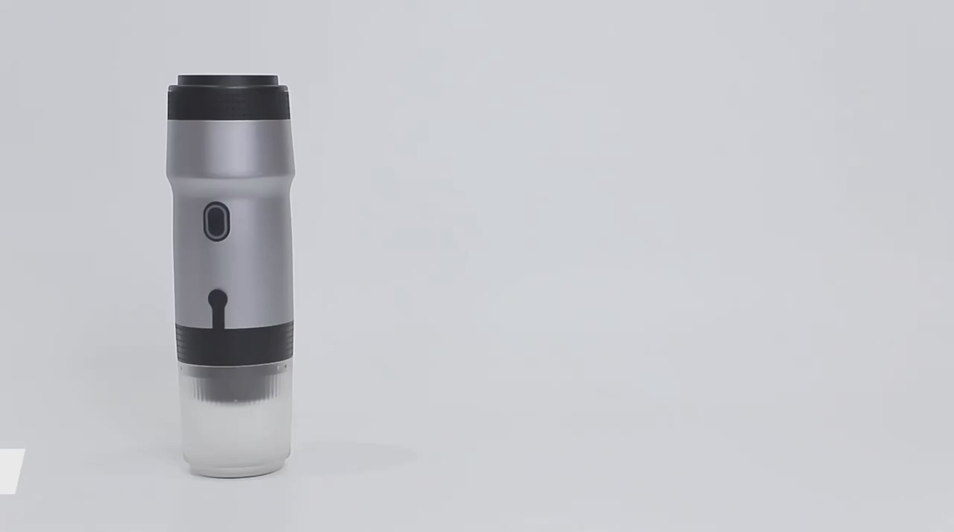 Demonstration of a portable espresso maker brewing a fresh cup of coffee from a small coffee capsule on a rocky beach at sunset.