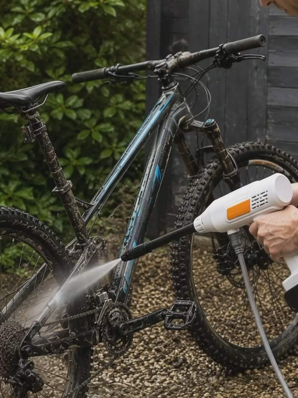Video showing a man using a portable cordless pressure washer drawing water from a bucket to blast mud off a mountain bicycle.