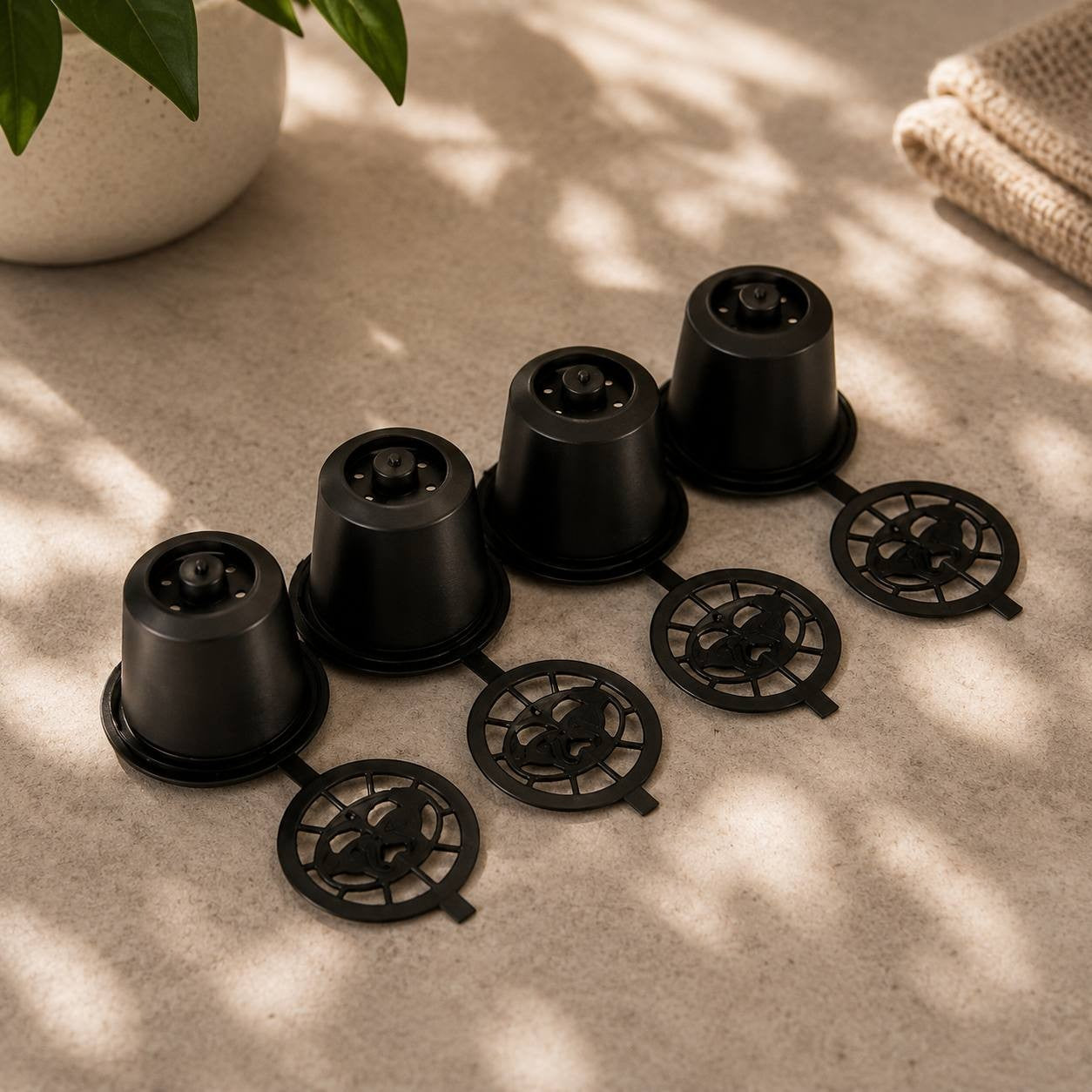 A row of four reusable black plastic coffee capsules with round mesh bases on a stone surface.