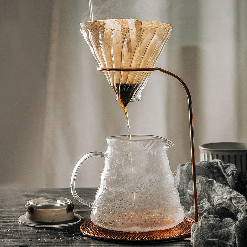 Coffee being poured from a paper filter into a glass carafe on a wooden table.