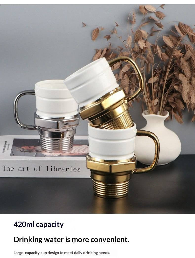 An eye-catching display of the glow plug mug set, with a silver mug on a book and two gold mugs stacked, emphasizing their stackable feature and 420ml capacity, with dried flowers in a vase.