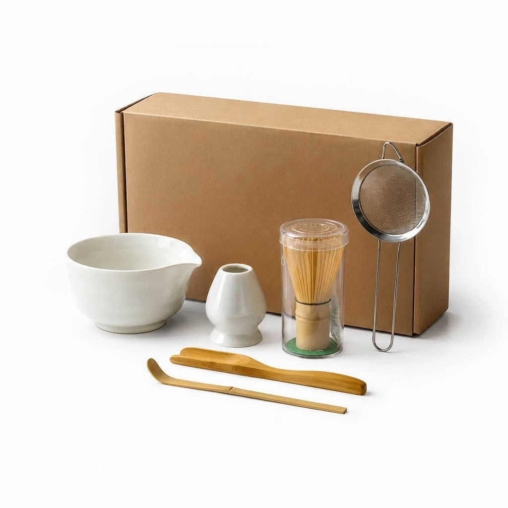 Complete matcha tea set with white ceramic bowl, bamboo whisk, wooden scoop, and metal strainer arranged on white background.