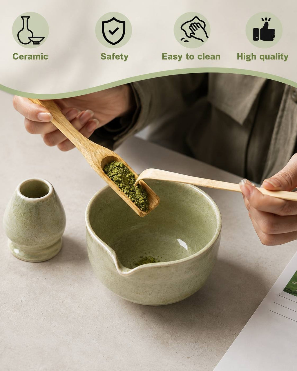 Close-up of hands using a wooden bamboo scoop to add matcha powder into a green ceramic tea bowl.
