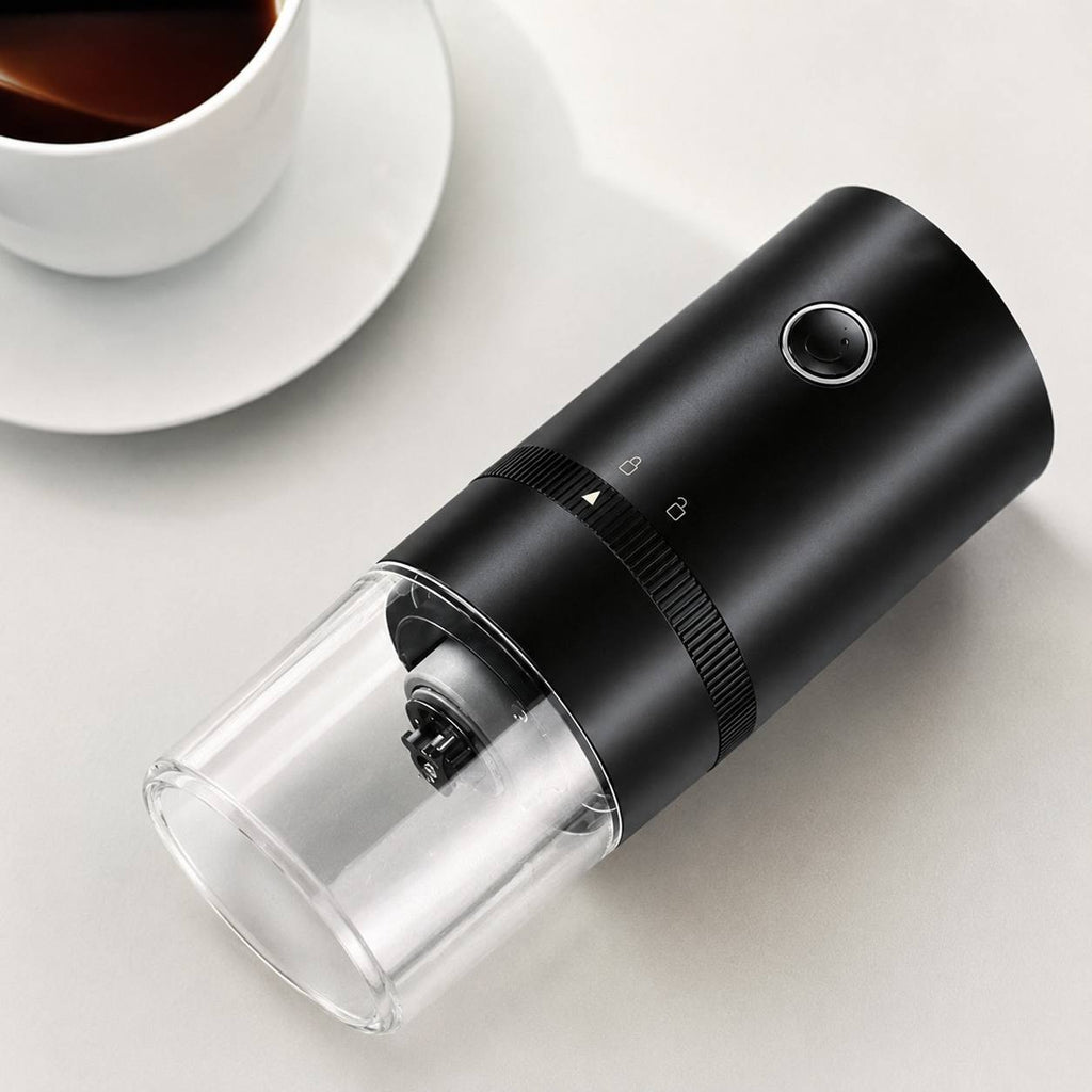A sleek rechargeable electric coffee grinder sitting on a table next to a coffee cup.