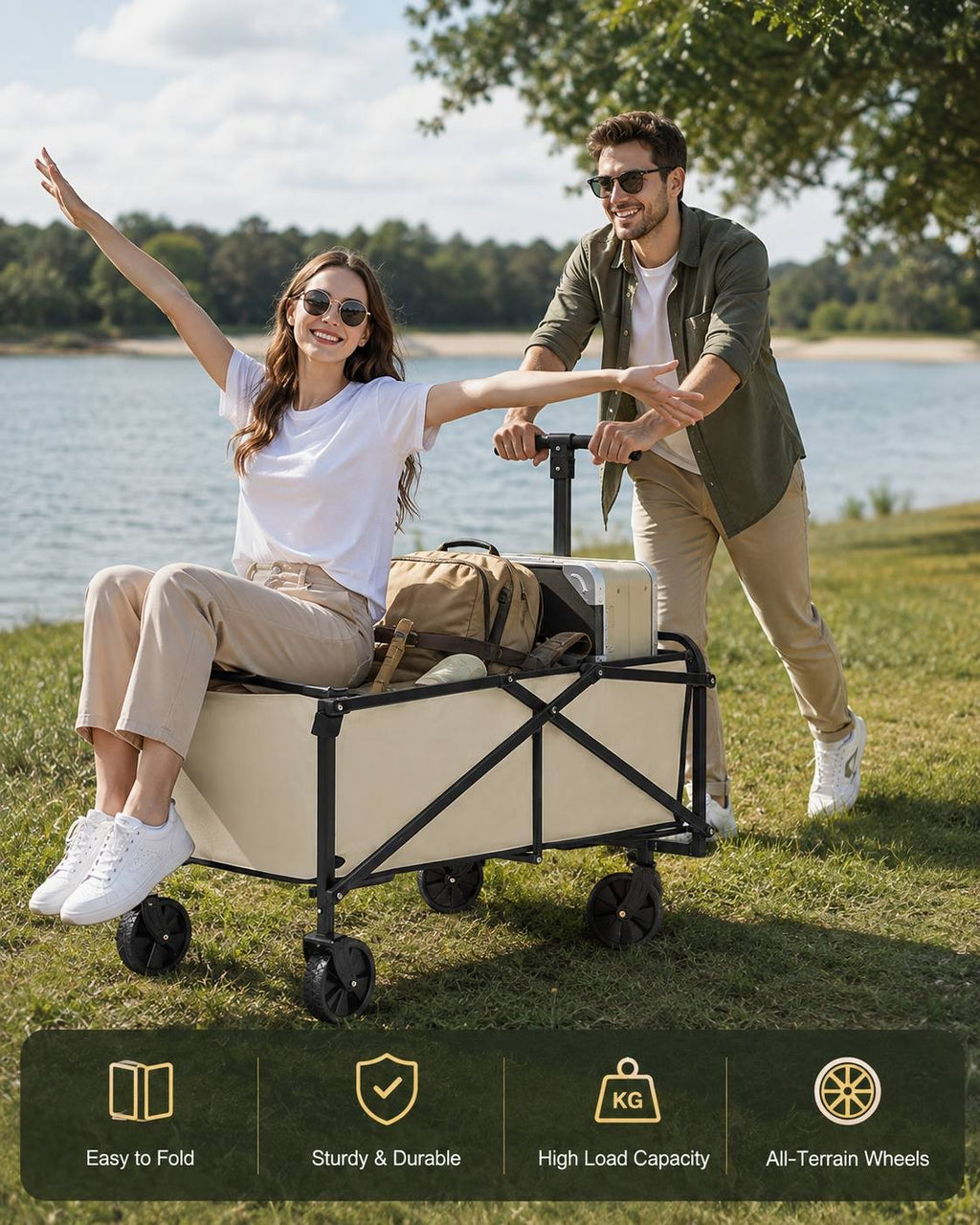 Woman sitting happily inside a loaded beige utility wagon with her arms outstretched, while a man pushes the cart along a grassy shore by a lake.