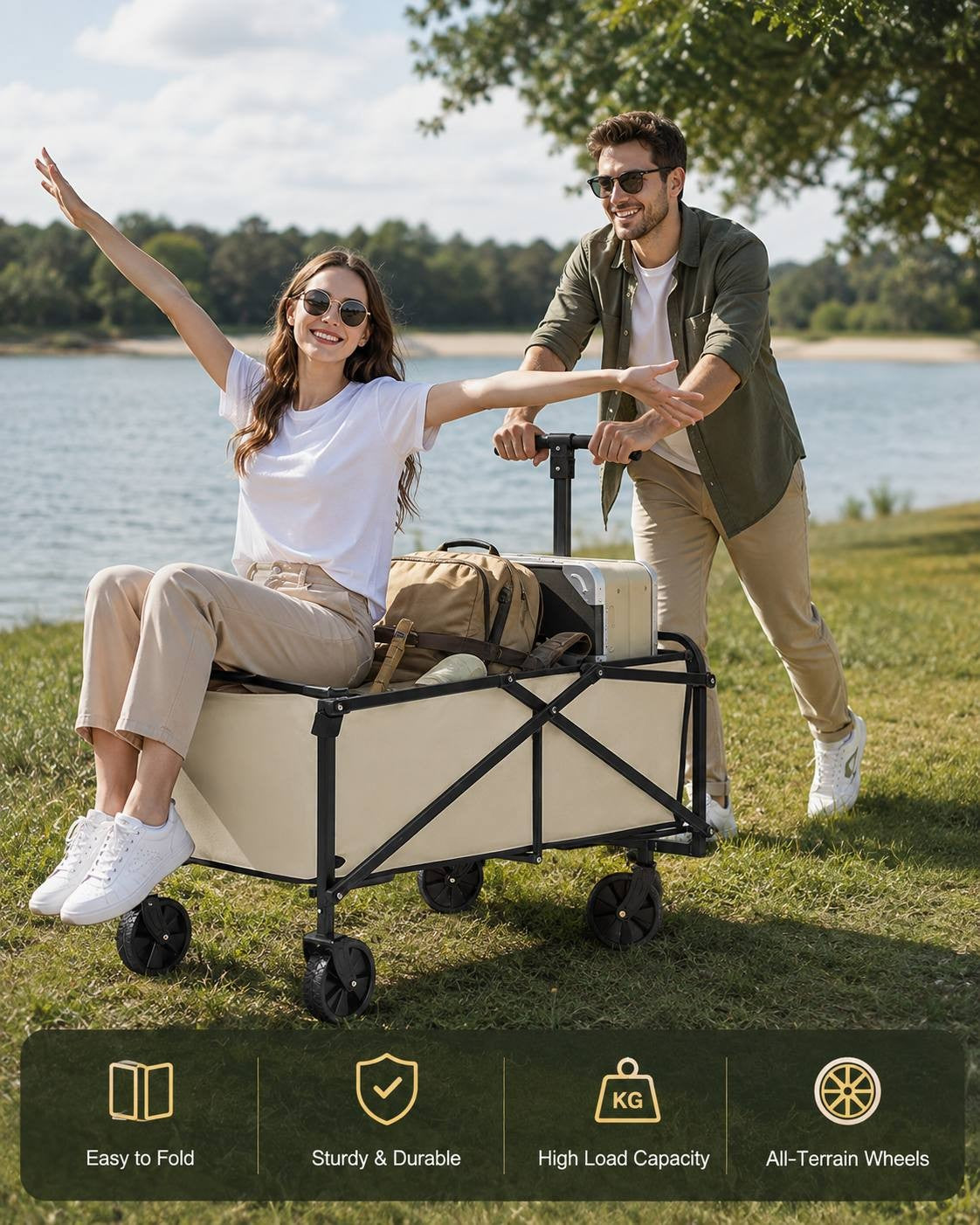 Woman sitting happily inside a loaded beige utility wagon with her arms outstretched, while a man pushes the cart along a grassy shore by a lake.